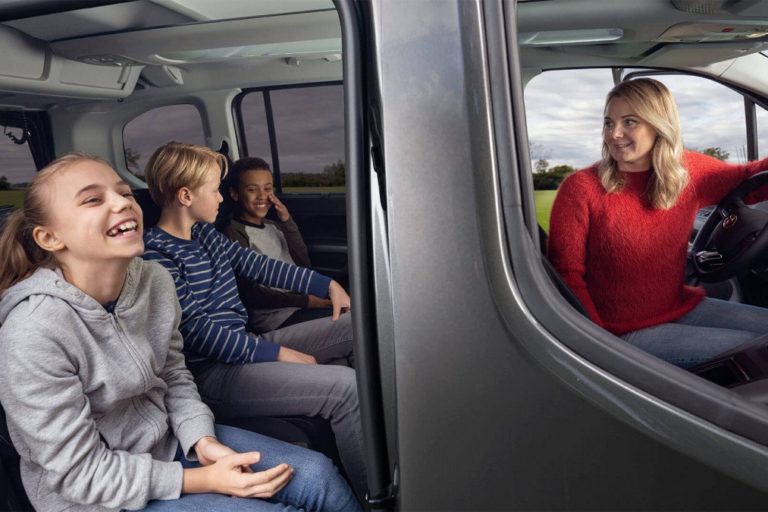 Maman dans sa Toyota Proace City Verso qui regarde ses trois enfants à l'arrière rassurée parce qu'elle a une bonne assurance auto