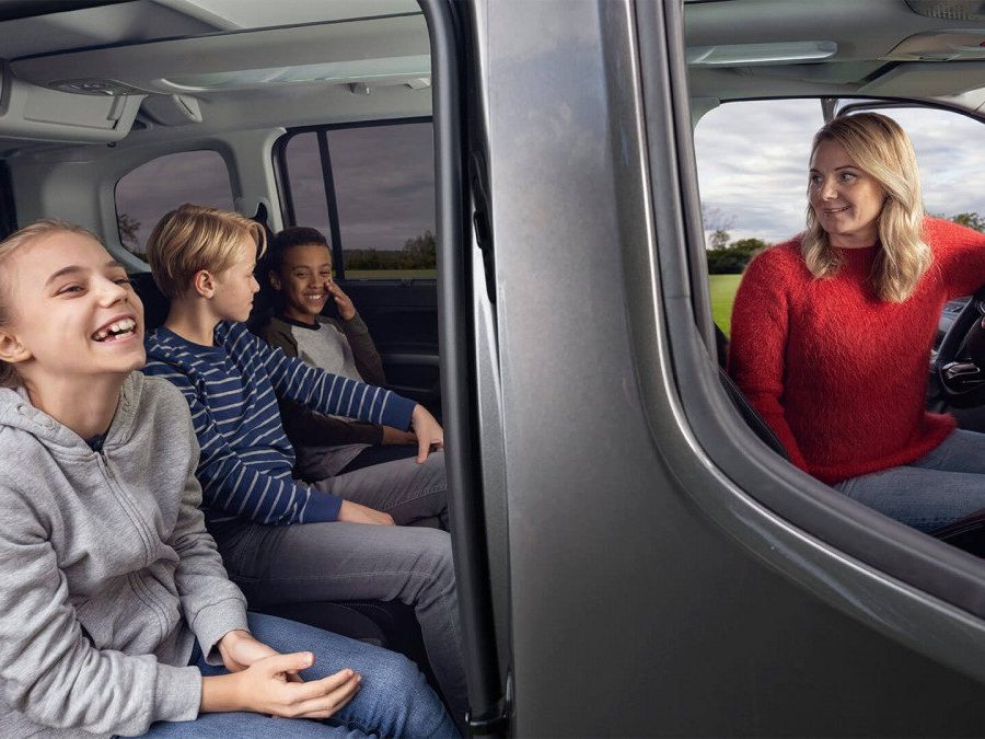 Maman dans sa Toyota Proace City Verso qui regarde ses trois enfants à l'arrière rassurée parce qu'elle a une bonne assurance auto