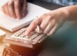 Homme assis à un bureau avec un cahier ouvert et une calculette en train de calculer la fiscalité de sa voiture de société