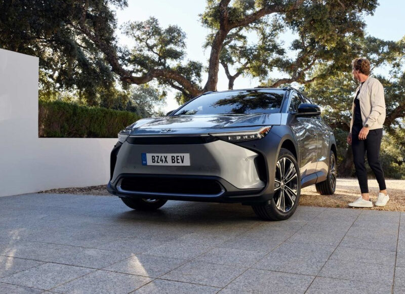 toyota-bz4x-2021-gallery-02-full_tcm-3027-2384025 1 Toyota BZ4X grise garée sur la coure d'une maison avec un homme montant dans le siège conducteur