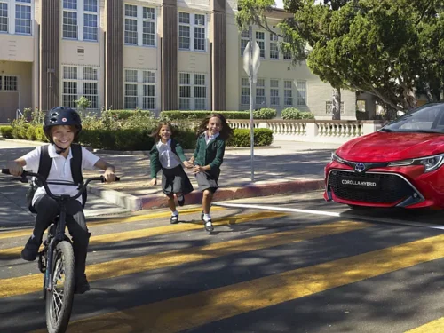 Voiture Toyota Corolla hybride rouge à l'arrêt devant un passage pour piéton avec des enfants qui traversent